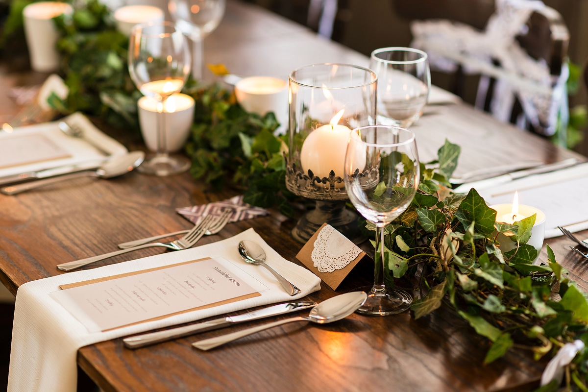 Table de mariage romantique avec menu "Svadobné menu", guirlande de lierre vert et bougies allumées sur une table en bois.