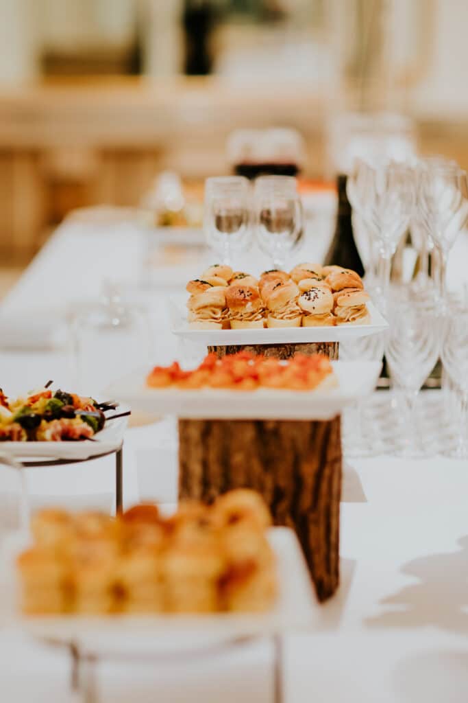 Assortiment d'amuse-bouches et desserts variés sur une table de buffet blanc, avec mini-sandwichs, brochettes et verres.