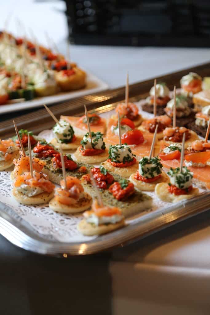 Canapés variés sur plateau: blinis saumon fumé, billes de fromage frais ciboulette, et tartines pesto. Prêts pour réception.