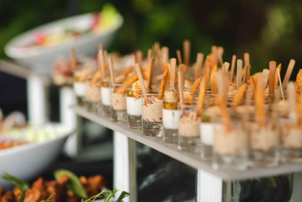 Range de verrines d'apéritif avec crevettes, sauces crémeuses et tuiles croustillantes sur un buffet de traiteur d'événement.