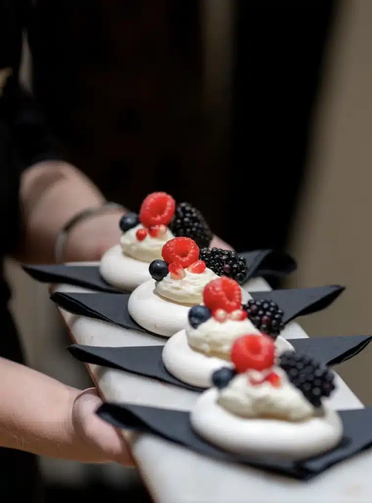 Serveur tenant un plateau de mini pavlovas blancs garnis de crème, framboises, myrtilles, mûres et graines de grenade.