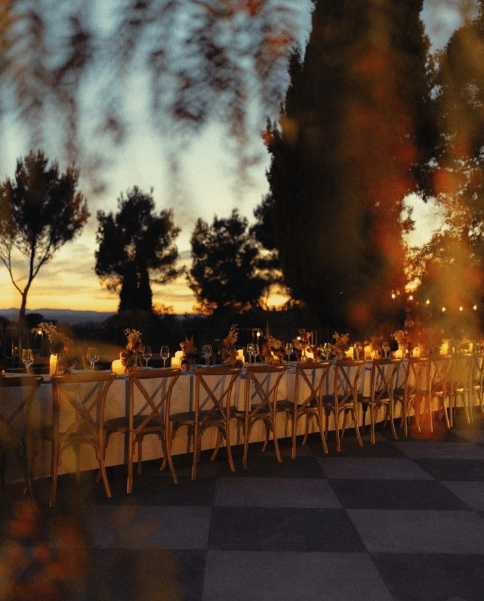 Dîner de mariage élégant en plein air avec bougies, fleurs et chaises en bois au coucher du soleil.