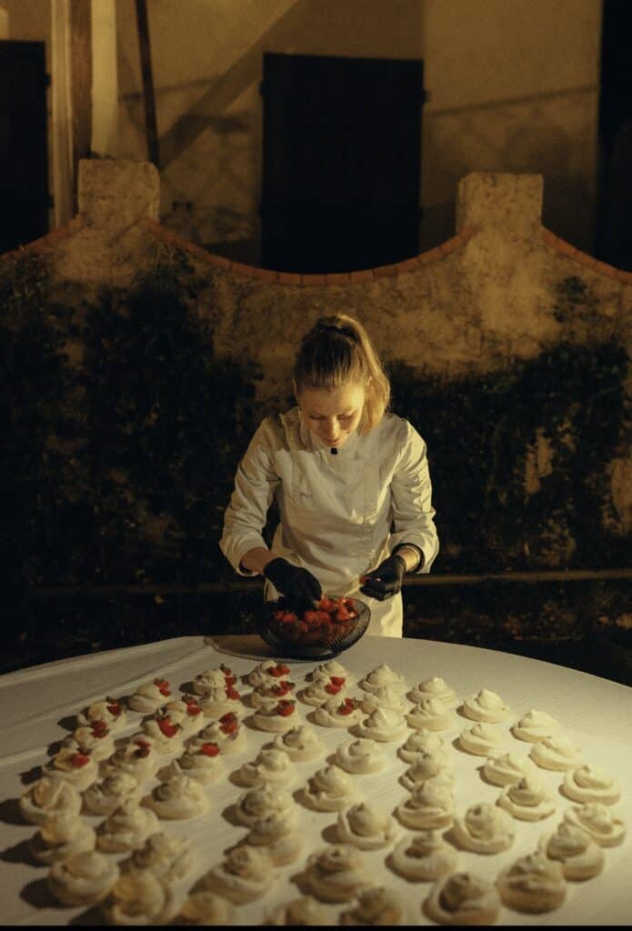 Chef pâtissière disposant des fraises fraîches sur des mini pavlovas lors d'un événement nocturne raffiné en extérieur.