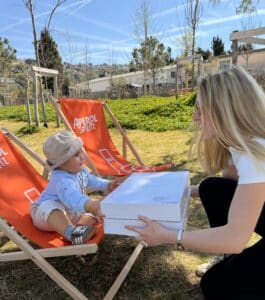 Femme offrant des boîtes à un bébé sur un transat orange Aperol Spritz en extérieur.