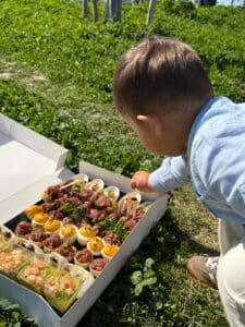 Enfant tendant la main vers un plateau de bouchées apéritives gourmandes lors d'un pique-nique ensoleillé.