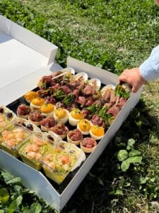 Coffret traiteur apéritif varié sur l'herbe. Main d'enfant saisissant une bouchée gourmande.